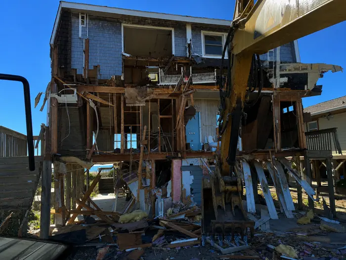 Excavator taking a two-story coastal home down to the pilings